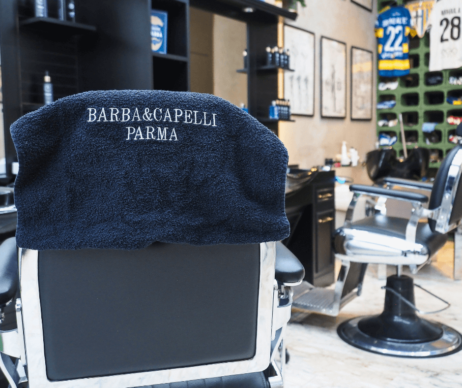 asciugamano-firmato-barba-e-capelli-parma-su-poltrona-sullo-sfondo-il-negozio-della-barberia-a-parma