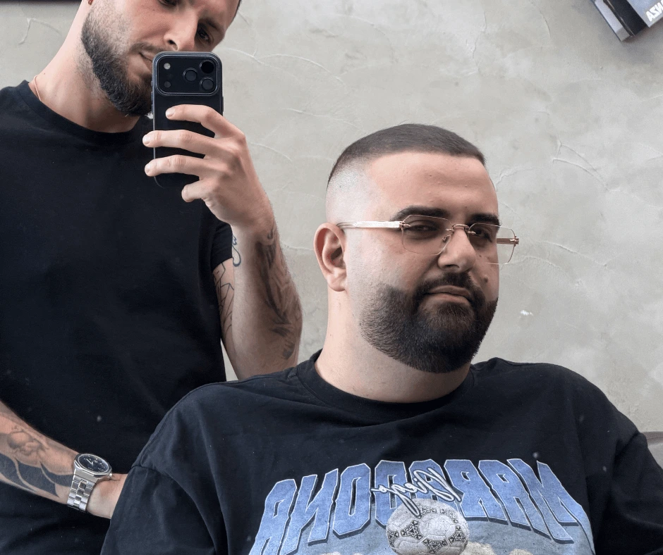 Cliente con occhiali, taglio corto sfumato e barba definita accanto al barbiere